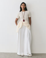 Person wearing a short-sleeve top with wide-leg pants and a long necklace.
