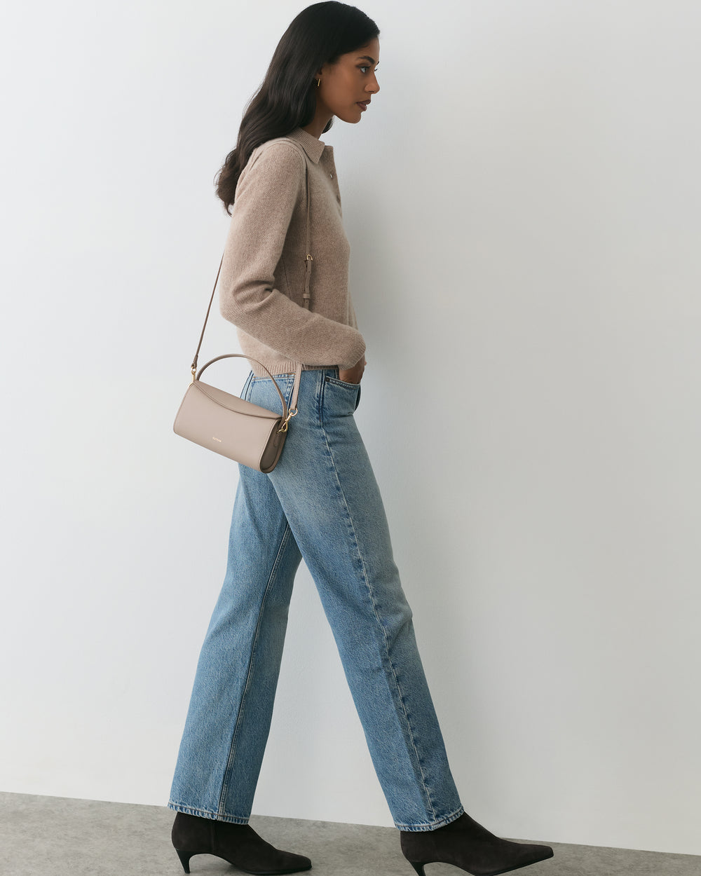 Person walking with a handbag, wearing a sweater, jeans, and boots.