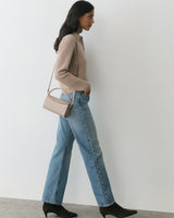 Person walking with a handbag, wearing a sweater, jeans, and boots.