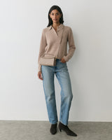 Person wearing a sweater, jeans, boots, and a shoulder bag, standing against a plain background.