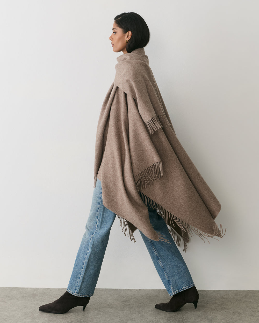 Person wearing a cape with jeans and boots walking indoors.