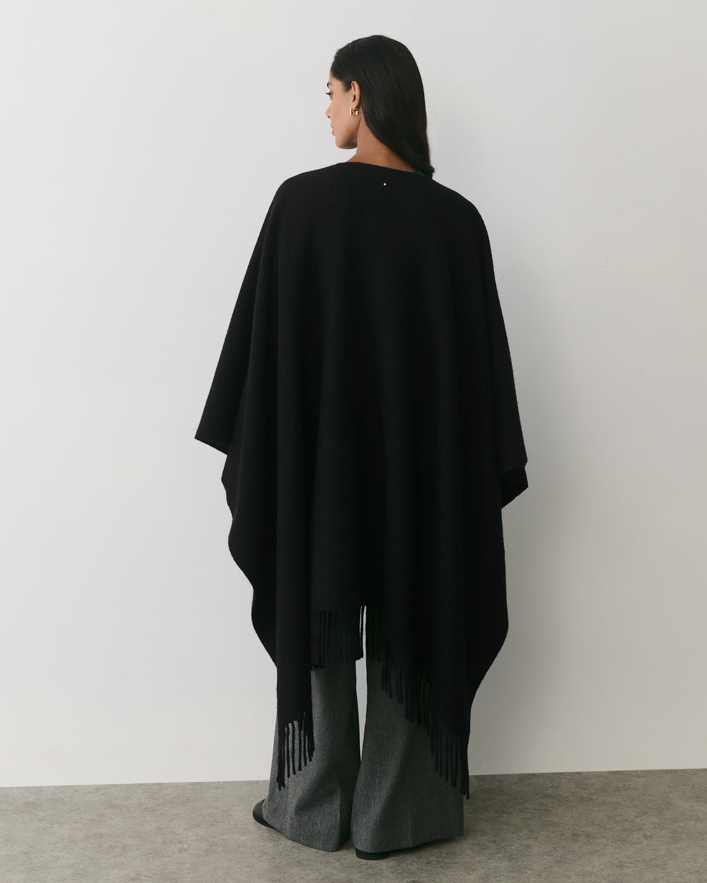 Person wearing a cape and wide-legged pants, standing against a plain wall.