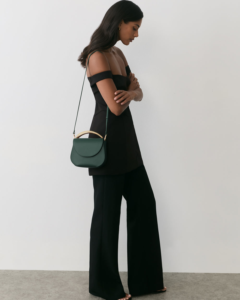 Woman in off-shoulder top and wide-leg pants with a shoulder bag.