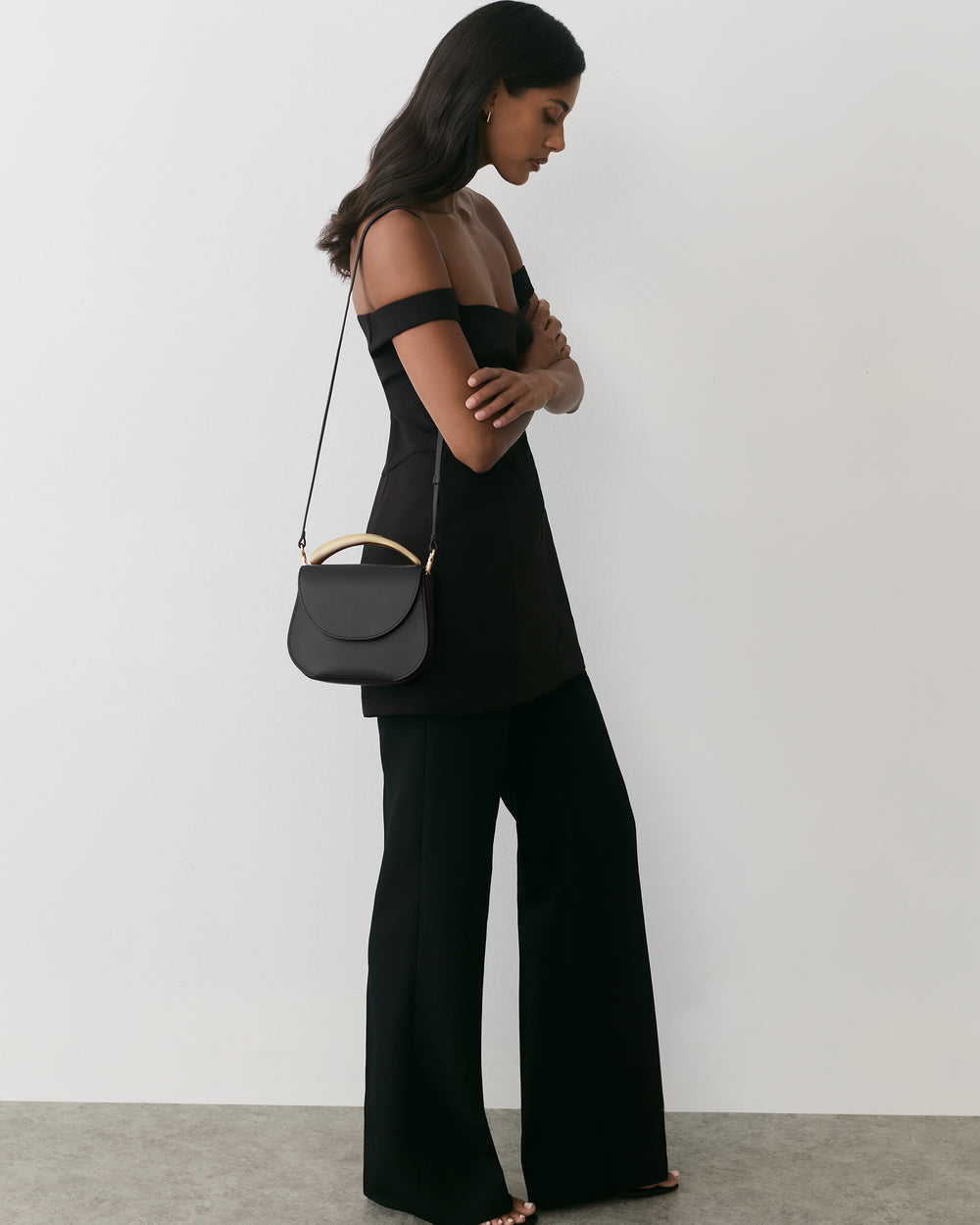 Woman in sleeveless top and pants with a handbag over shoulder standing sideways.