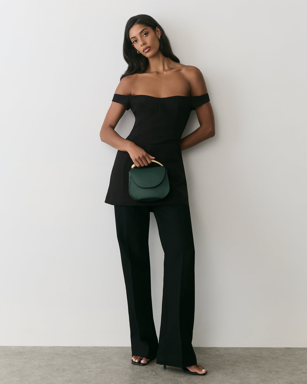 Person in strapless outfit holding a small purse, standing against a plain backdrop.