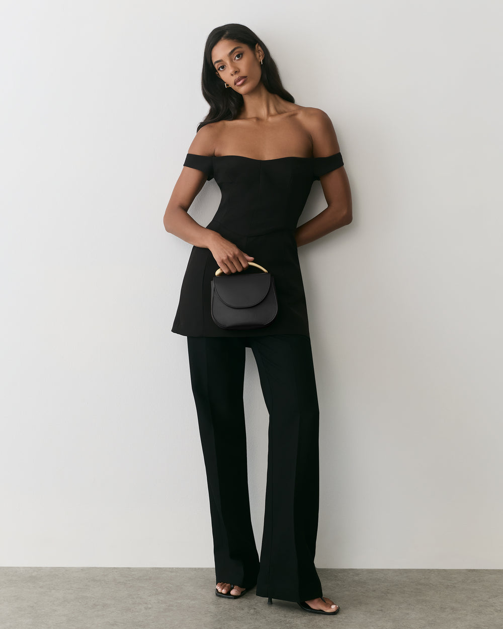 Person in off-shoulder dress with long pants holding a small purse.