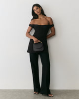 Person in off-shoulder dress with long pants holding a small purse.