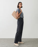 Person standing with a handbag over shoulder wearing a shirt and jeans.