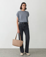 Person wearing casual outfit standing with handbag.