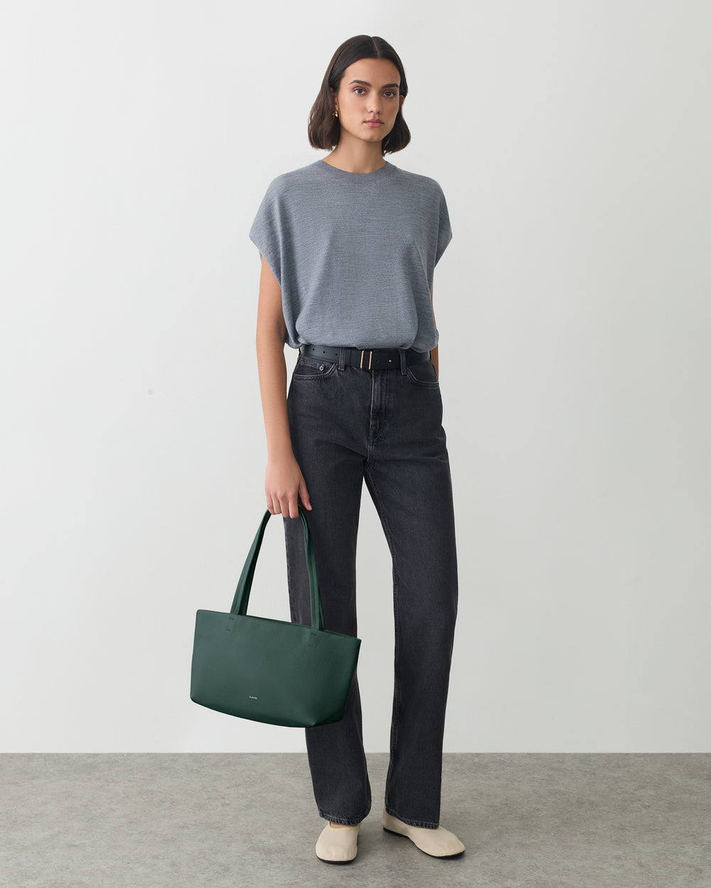 Person standing with a handbag wearing a t-shirt and jeans.