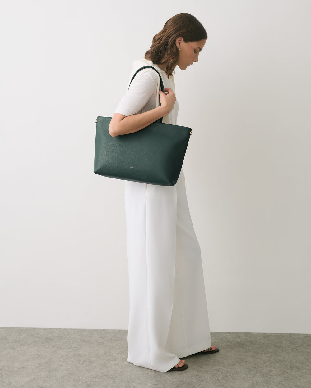 Person in side profile holding a large tote bag, wearing a short-sleeve top and wide trousers.