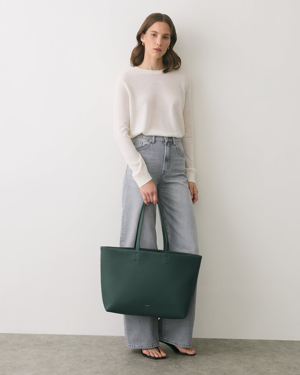 Person wearing long-sleeve shirt and jeans holds a large bag.