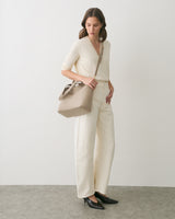 Person in casual outfit with shoulder bag and heels standing against plain background.