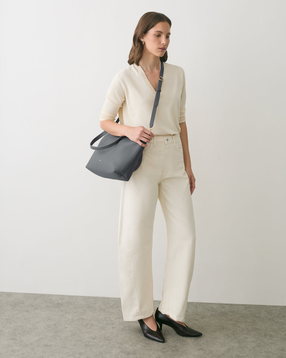 Person standing with one hand in pocket, holding a shoulder bag, and wearing casual clothes.