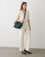Person standing with shoulder bag wearing long-sleeve top and wide-leg pants.