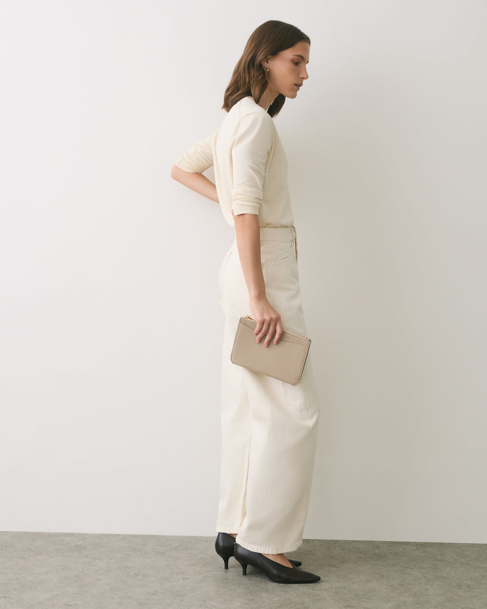 Person in outfit holding a rectangular clutch, standing sideways.