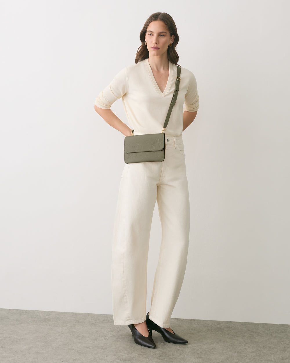 Person standing with a crossbody bag, wearing a long-sleeve top and wide-leg pants.