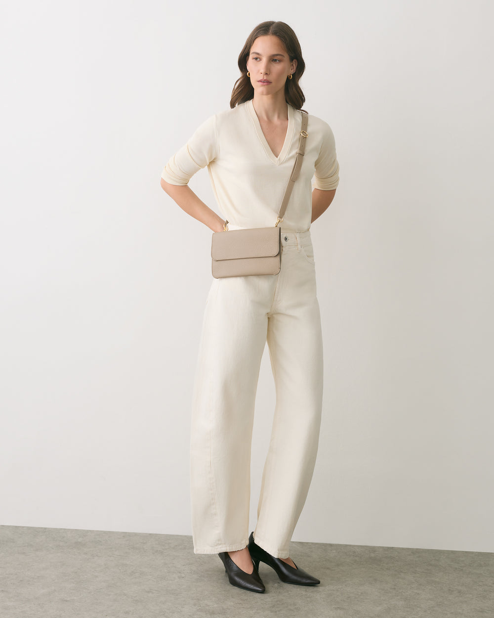 Person wearing a sweater and trousers with a crossbody bag and heeled shoes.