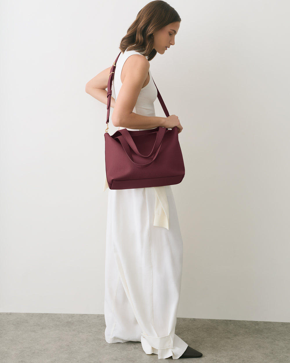 Person standing with one hand on a shoulder bag wearing a sleeveless top and long pants.