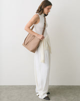 Person in sleeveless outfit carries shoulder bag and has sweater tied at waist.