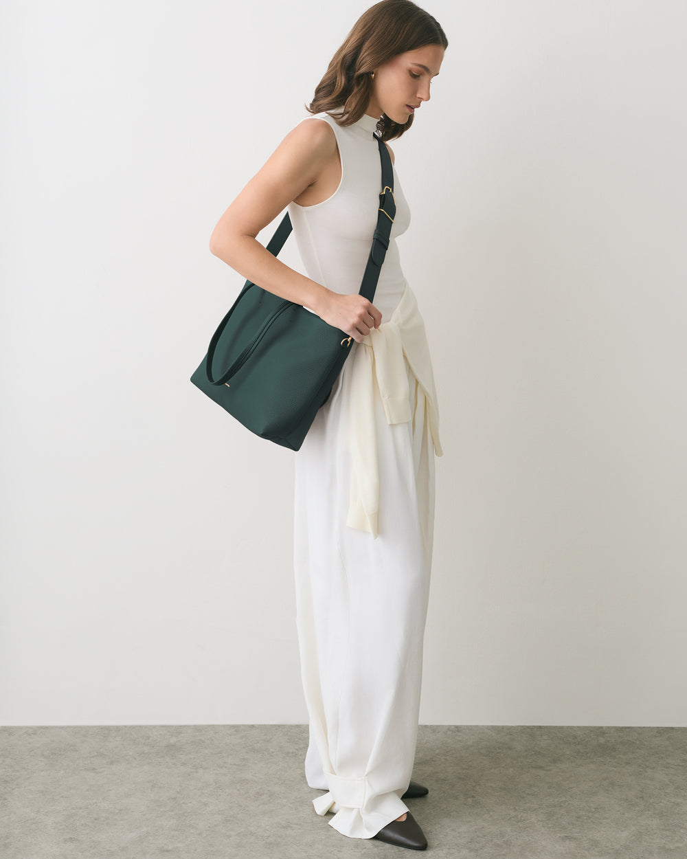 Person in long dress carries shoulder bag and sweater.