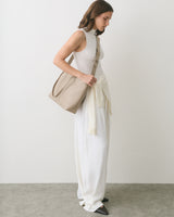 Person in a sleeveless top and long skirt, carrying a shoulder bag, with a sweater tied at waist.