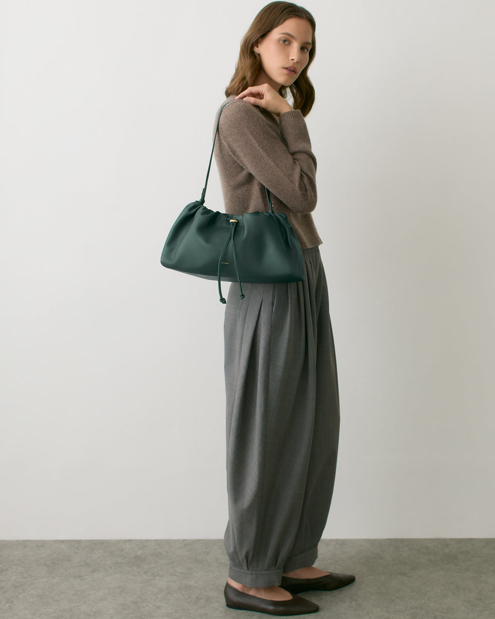 Person standing with shoulder bag, wearing long-sleeve top and wide-leg pants.
