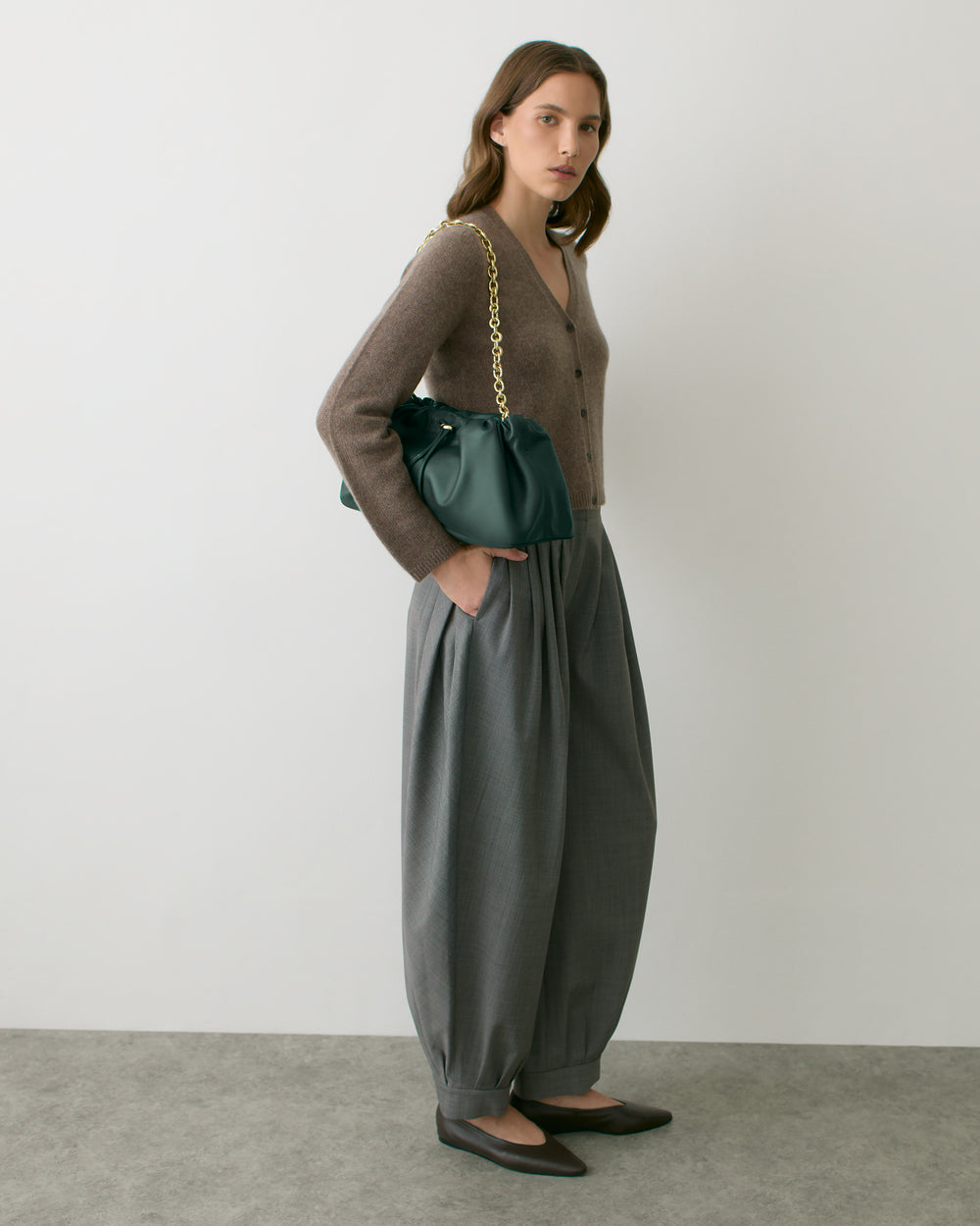 Person standing with a shoulder bag, hands in pockets, wearing a sweater and wide-leg pants.