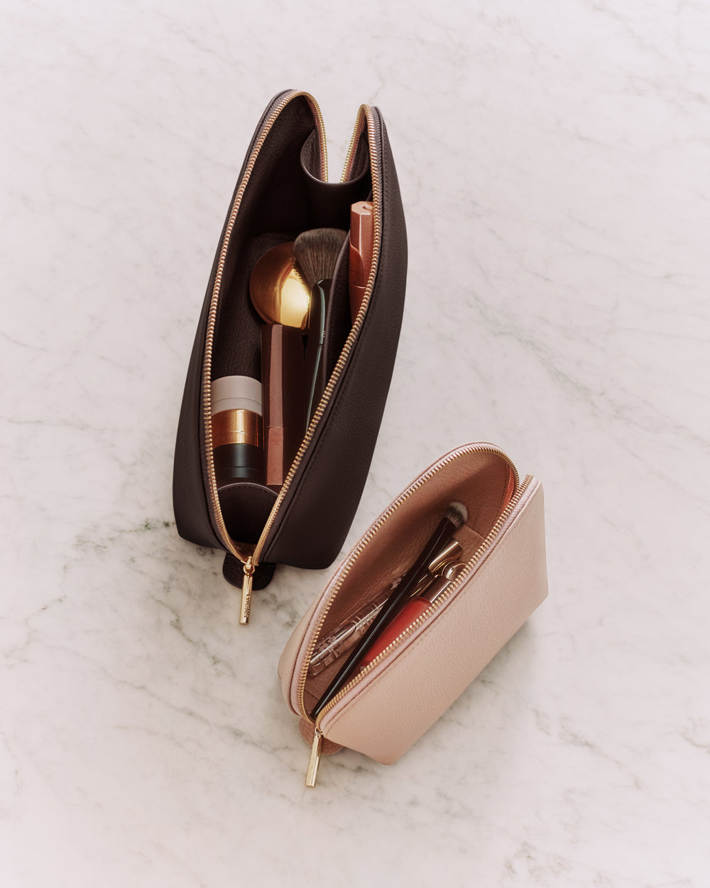 Two makeup bags on a marble surface, one open with brushes and cosmetics inside.