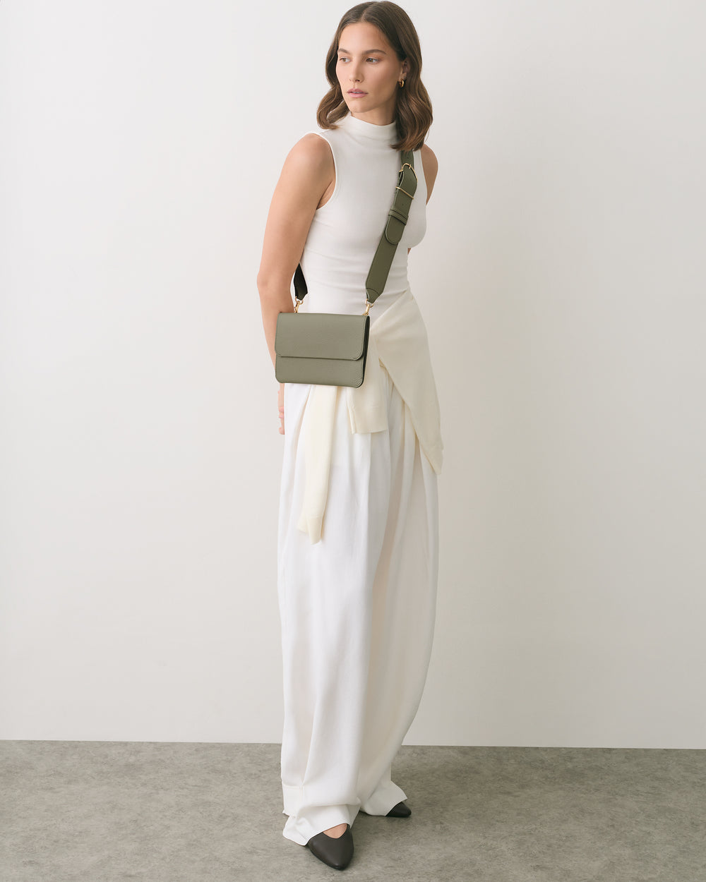 Person wearing sleeveless top and long skirt with a crossbody bag standing indoors