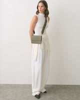 Person wearing sleeveless top and long skirt with a crossbody bag standing indoors