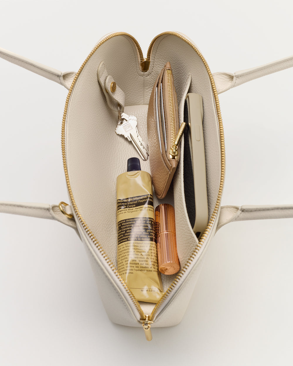 Open handbag showing keys, wallet, phone, lotion, and lipstick inside.