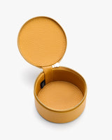 Round textured leather jewelry box with an open lid.