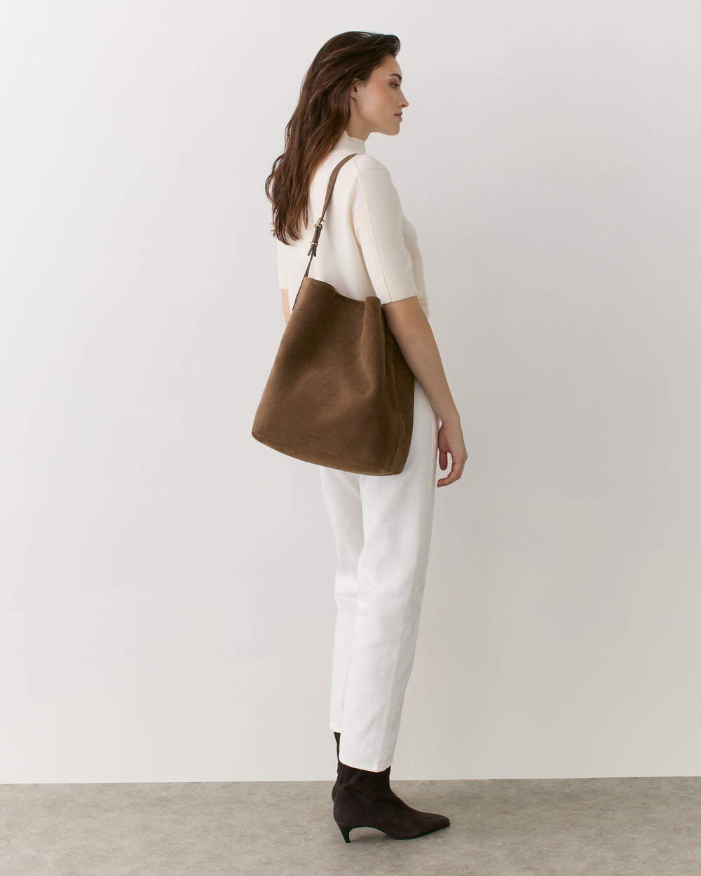Person standing with a shoulder bag, wearing a short-sleeved top and pants, facing left.