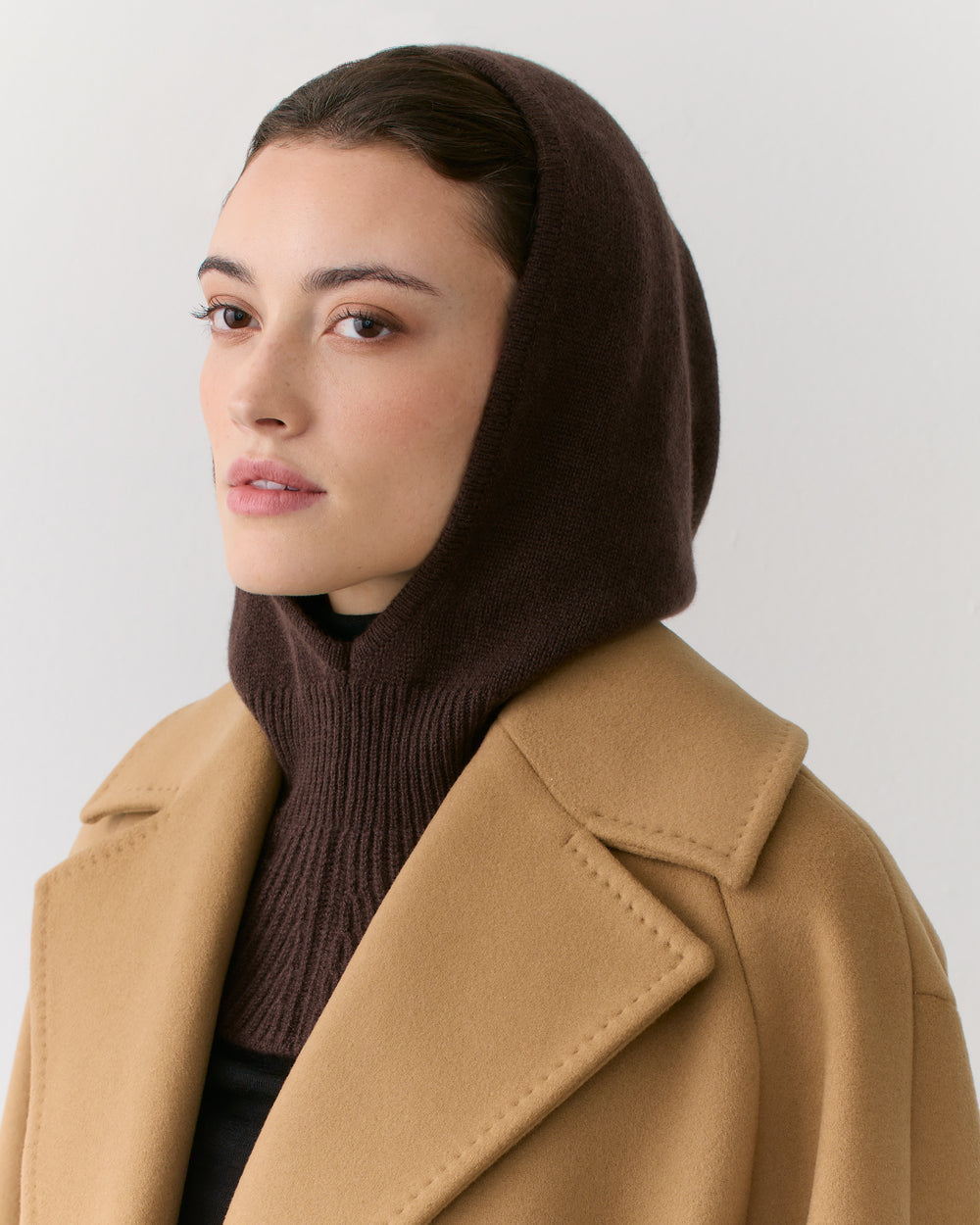 Person wearing a hooded garment and a coat, looking to the side.