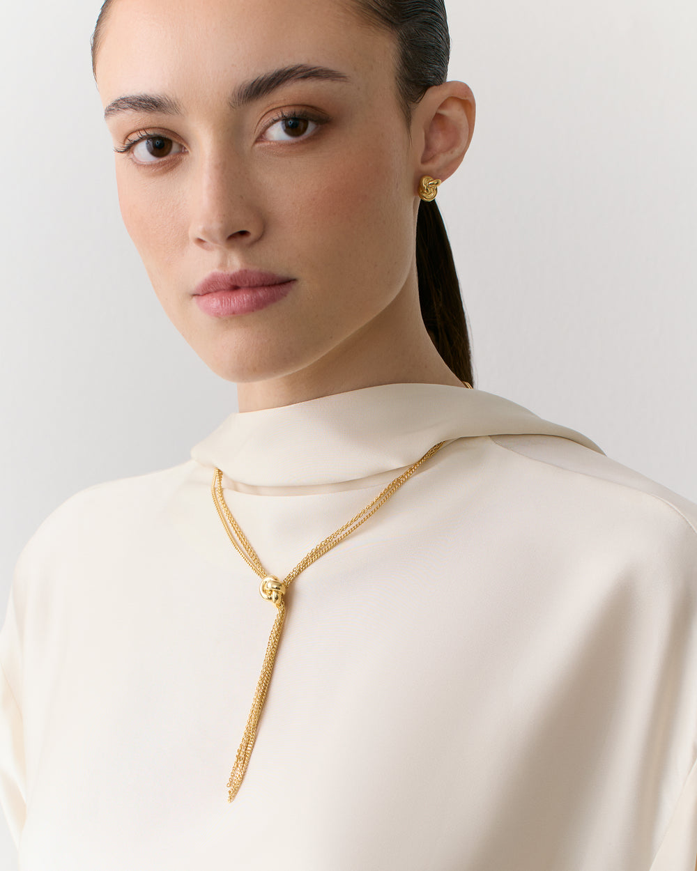 Person wearing a top with a gold necklace and earrings.