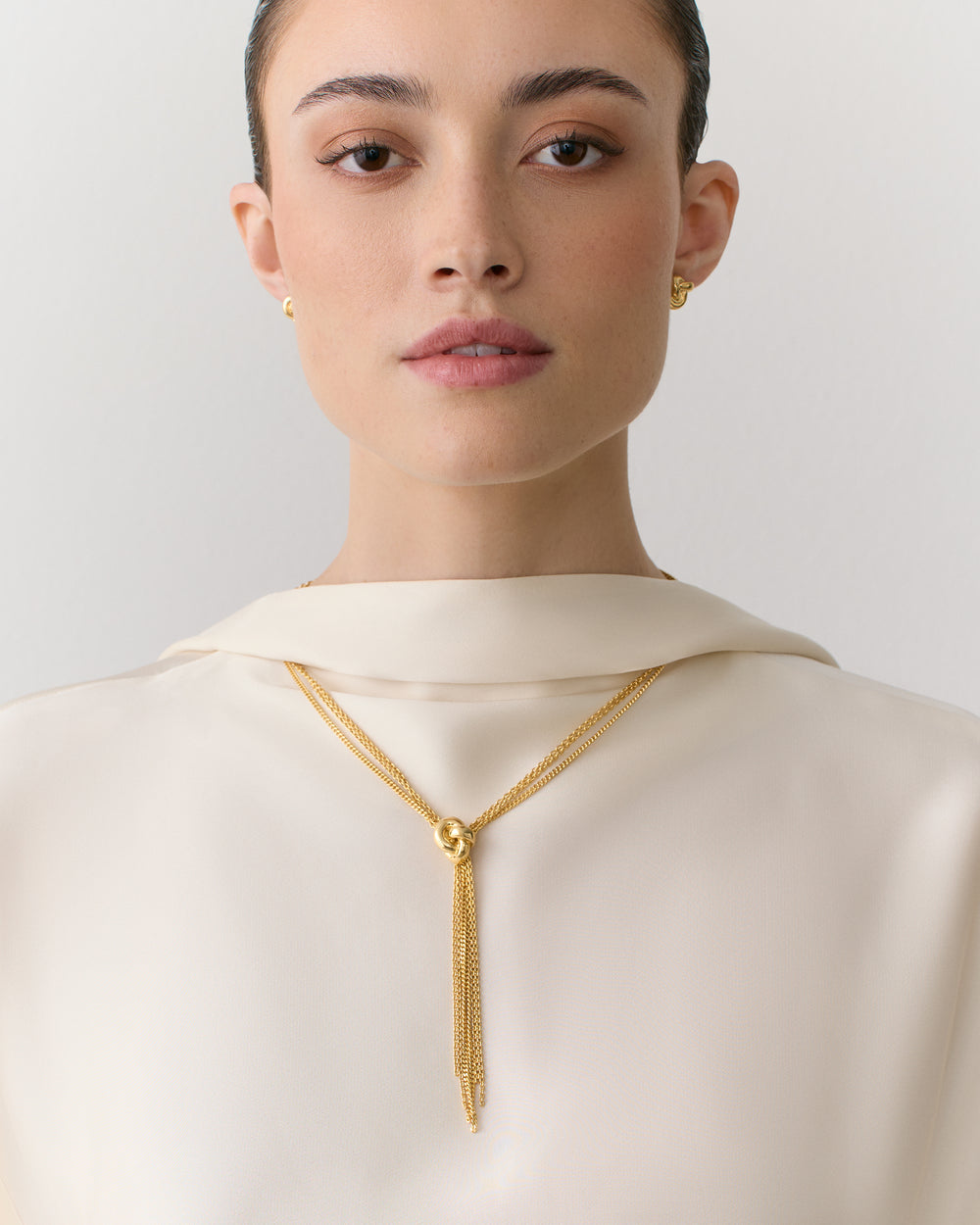 Person wearing a top with a necklace and earrings.