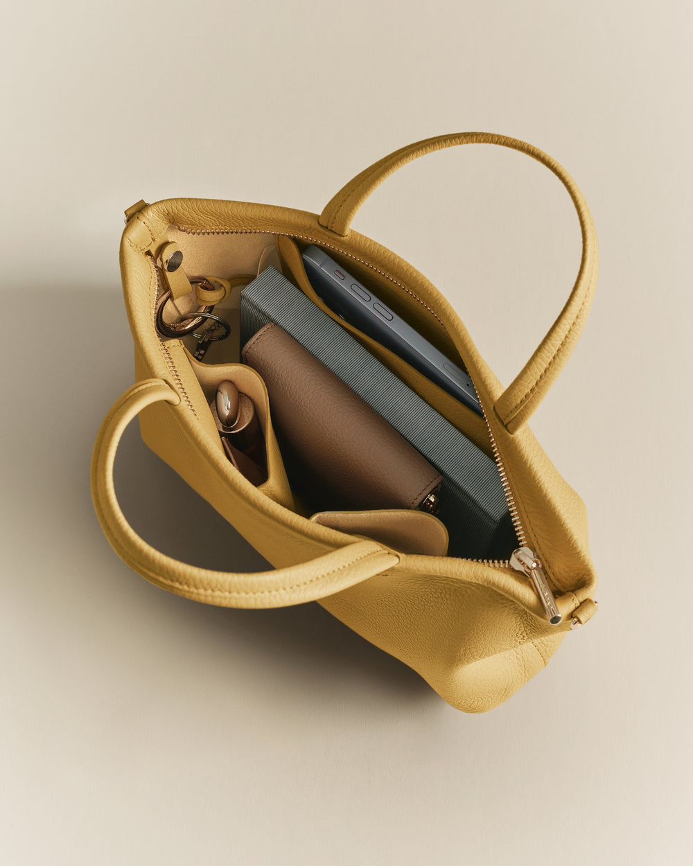Open handbag with items inside including a book, bottle, and pouch.