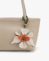 Handbag with a floral charm attached near the handle.