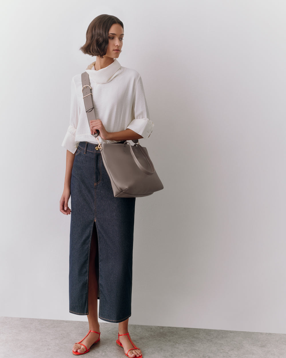 Person wearing a long skirt and top, holding a shoulder bag, standing indoors.