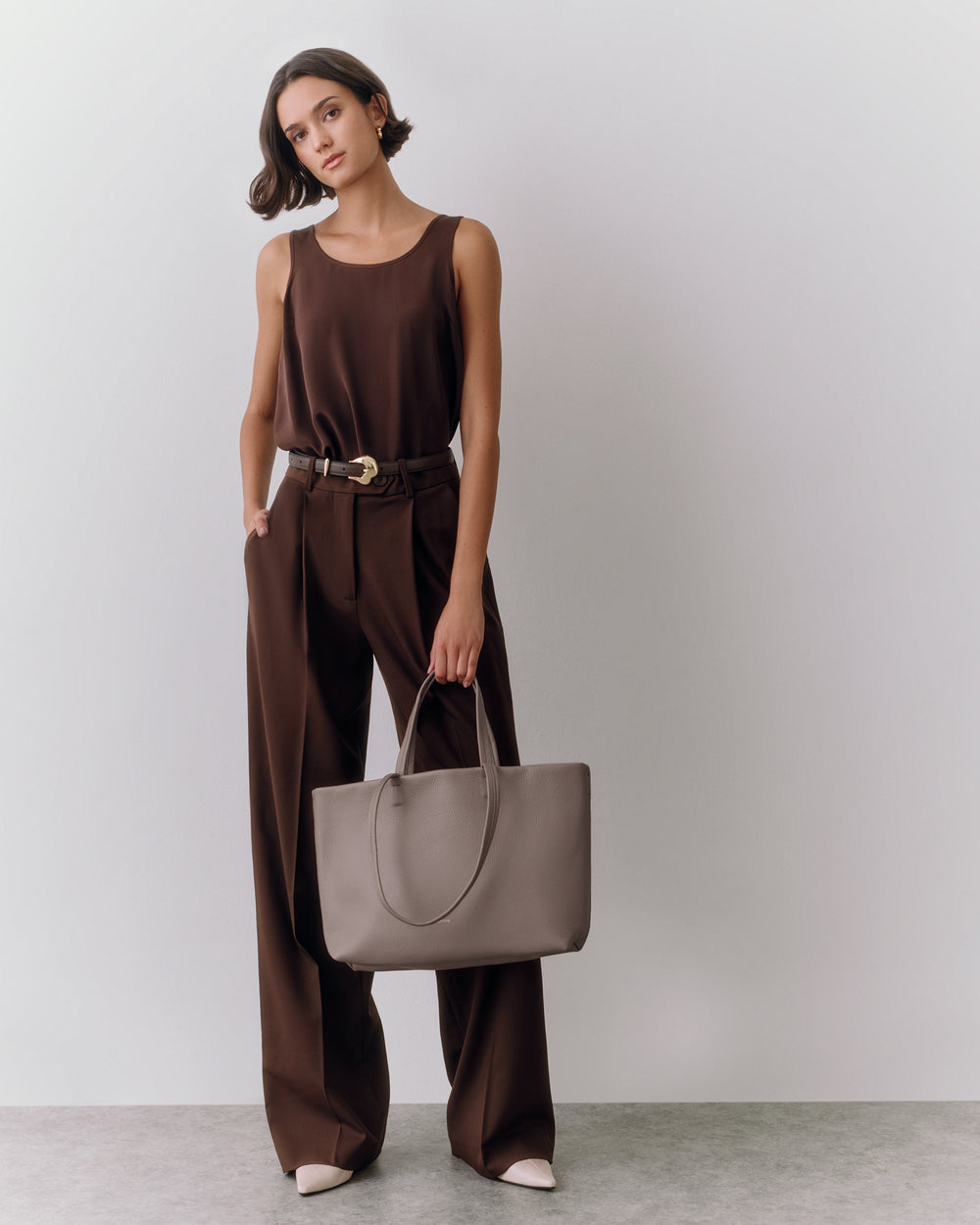 Person standing with large handbag wearing sleeveless top and trousers.