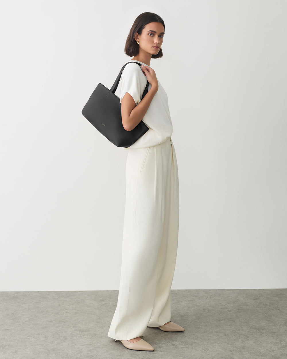 Person holding a shoulder bag wearing a top and wide-leg trousers.
