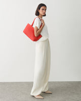 Person in light outfit holding a large handbag over shoulder.