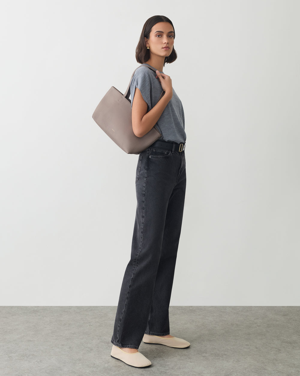 Person in casual outfit holds a handbag on shoulder.