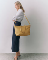 Person in white shirt and long skirt holding a large handbag over shoulder.