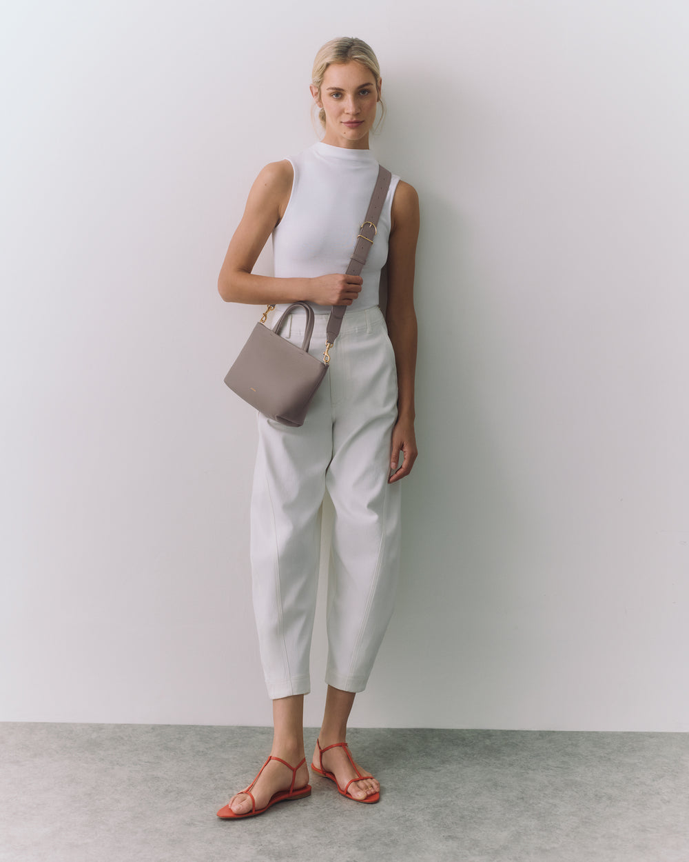 Person in sleeveless top and pants holding a small handbag over shoulder.