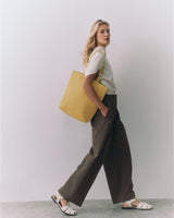 Person walking with a large tote bag and wearing sandals and wide-leg pants.