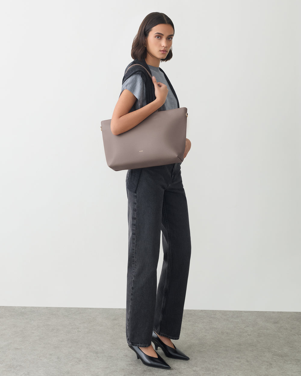 Person standing with a large shoulder bag, wearing a t-shirt and jeans.