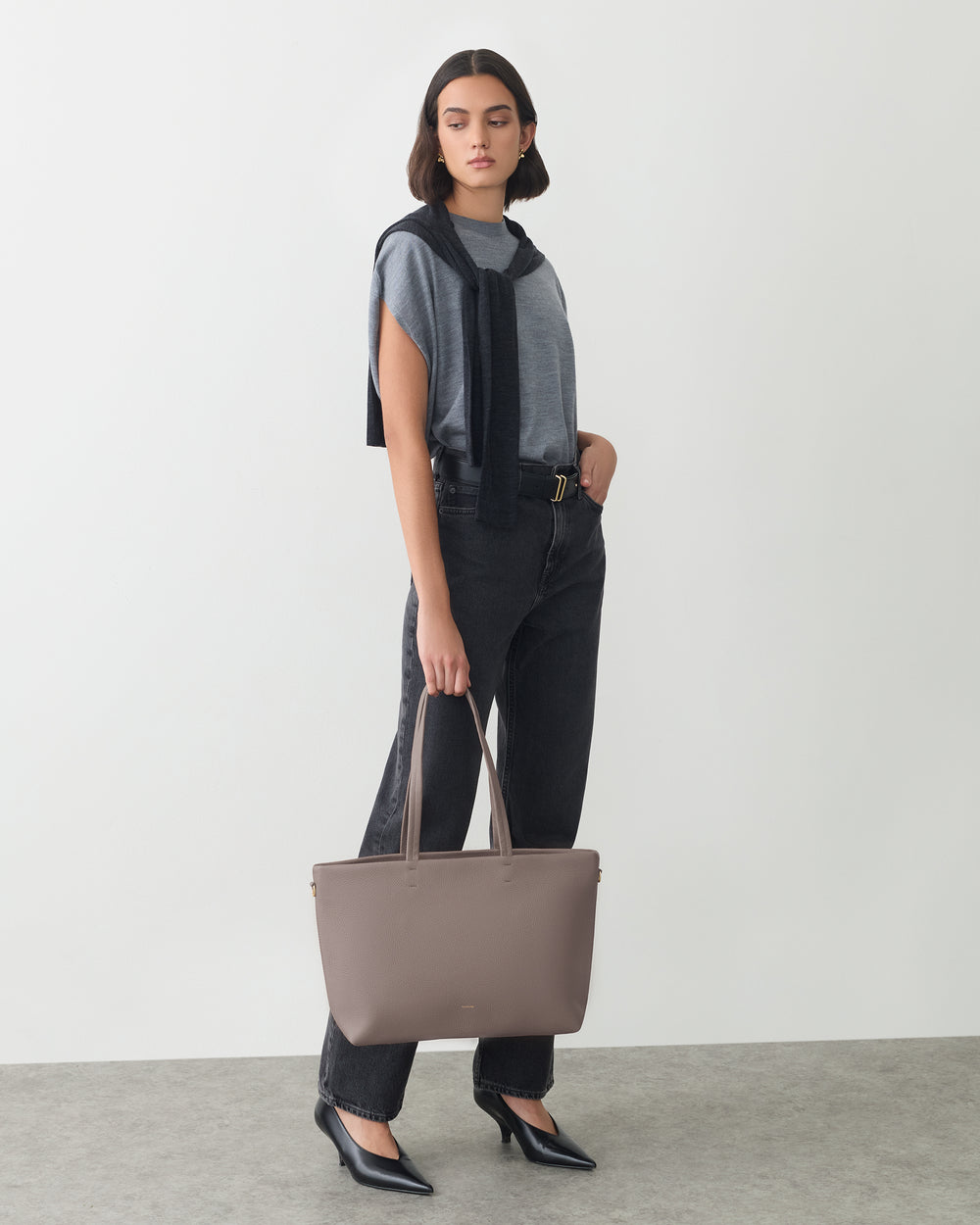 Person posing with large handbag in one hand and wearing casual outfit with cape draped over shoulders.