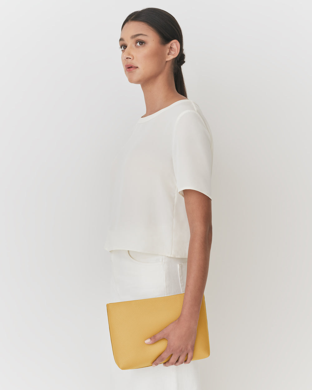 Person holding a clutch under one arm, wearing a short-sleeve top and looking to the side.